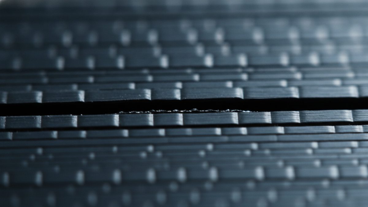 A macro close-up of dark gray layers stacked edge-on, with a dark horizontal gap separating two of the layers across the middle of the frame while the rows above and below fade out of focus.