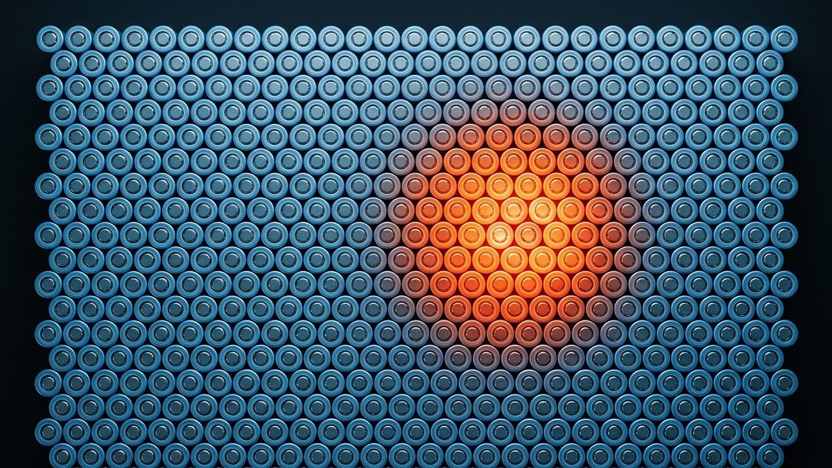 Hundreds of cylindrical battery cells, seen end-on and packed in a tight grid against a dark background, glow orange at the center, with the glow fading outward into cool blue-gray cells.